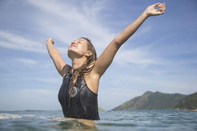 Woman standing chest deep in the sea with her arms raised and head tilted back